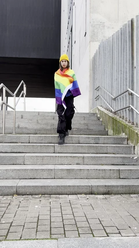 Vertical video of a young man walking down stairs showing off the pride flag. Stock Footage 259853318