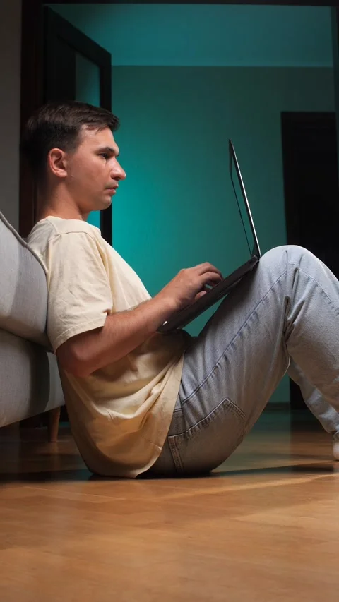 Vertical video young man working remotely on a laptop, sitting comfortably on Stock Footage 342772137