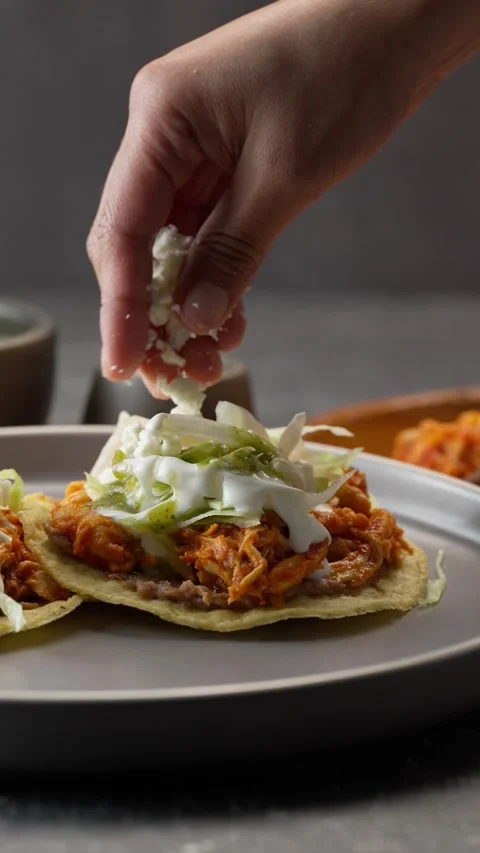 Vertical video, a young Mexican woman's hand spreads crumbled cheese on a toast Stock Footage 282549252