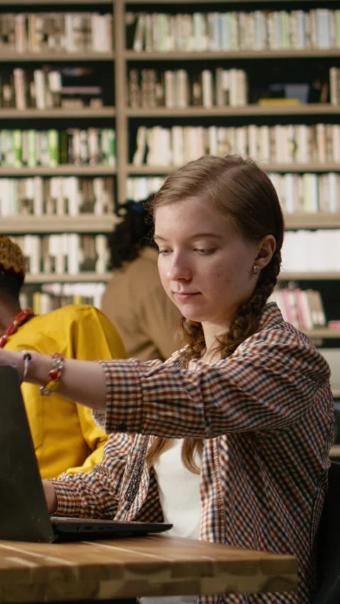Vertical Video Young student working on laptop taking notes at library table Stock Footage 337529481