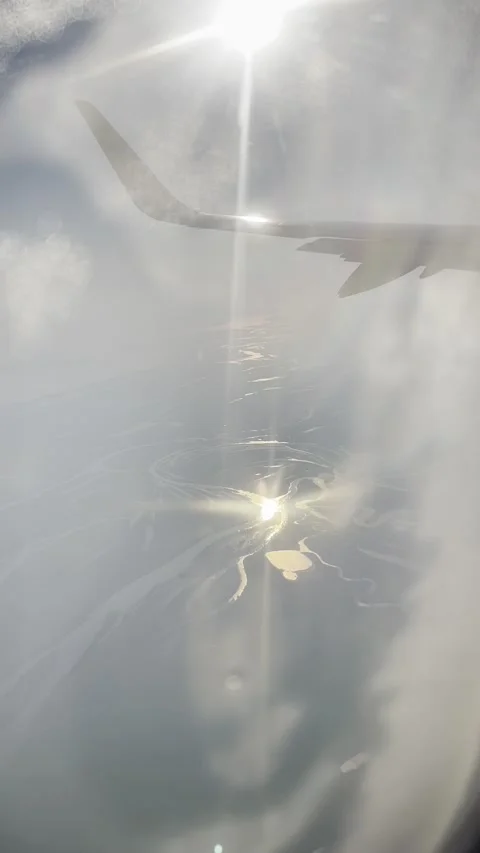 Vertical view from above of river through cloudy sky from blurred plane porthole Stock Footage 293971245