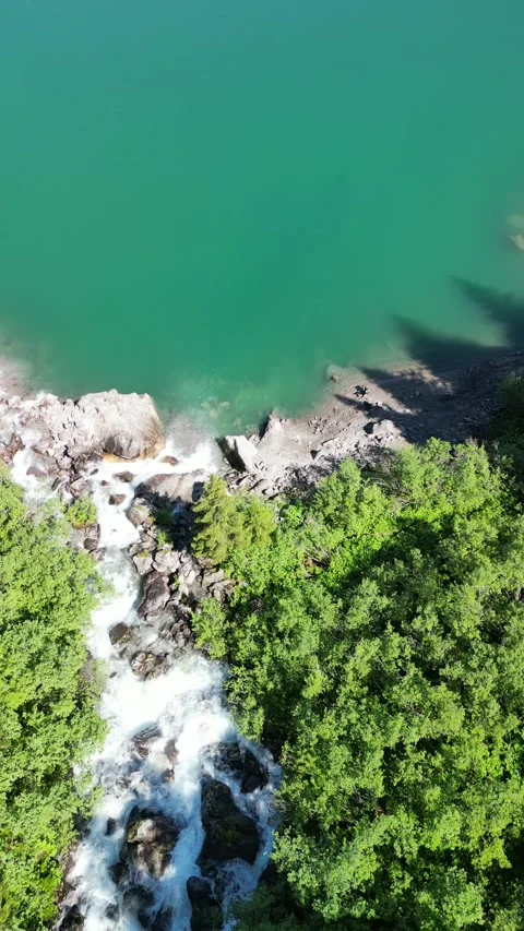 Vertical view of alpine lake with waterfall and forest in mountain valley Video stock 330749150