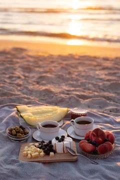 Vertical view of beach picnic with coffee, cheese, olives and melon at sunset. Stockfoto's