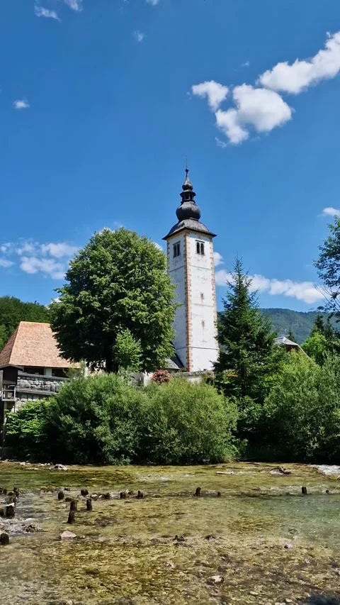 Vertical View of Catholic Church Tower by River, Outflow of Lake Bohinj Stock Footage 340925935