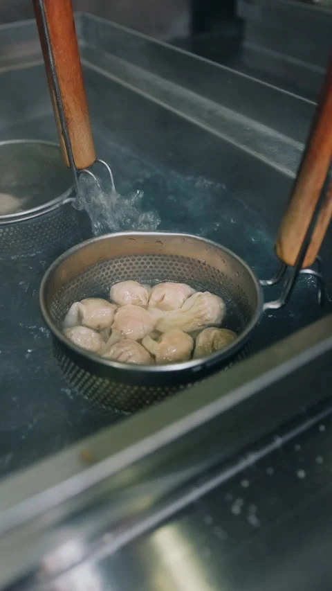 Vertical view of Chinese dumplings boiling in a metal strainer in hot water Stock Footage 333893370