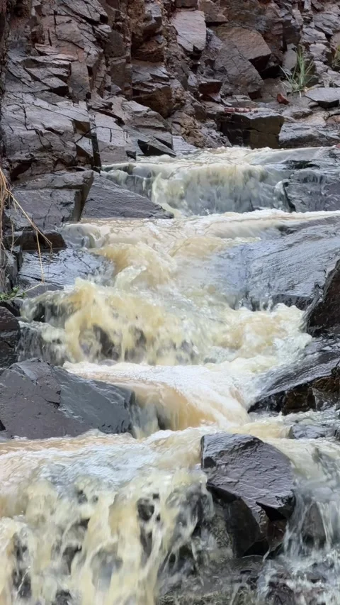 Vertical view of cloudy rainwater rushing across rocks in a narrow mountain Vidéo 332985872