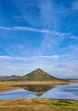 Vertical View of a Conical Hill Reflected in Still Reservoir Water Under Stock Photos