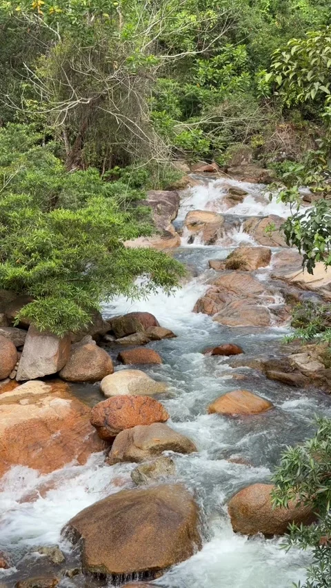Vertical view of a fast flowing river moving between large stones, with hillside Stock Footage 331725741