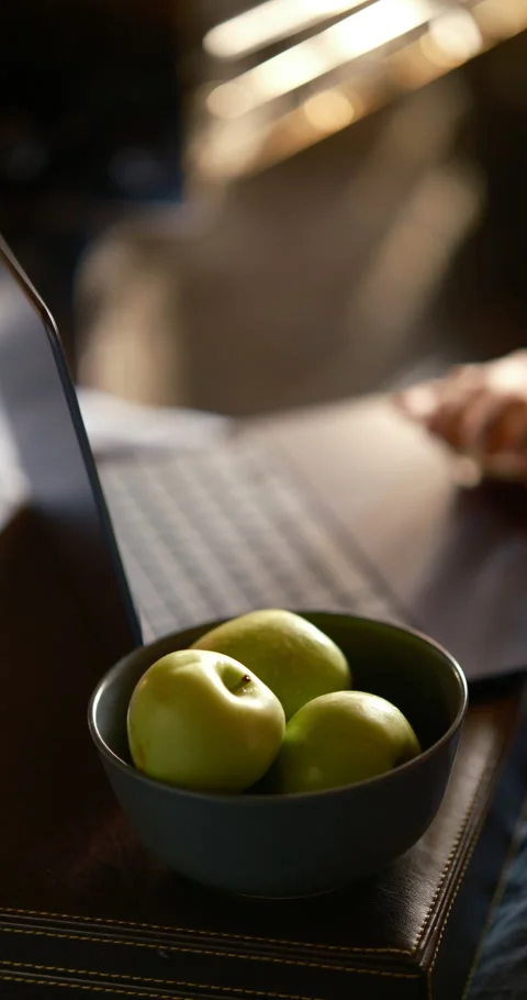 Vertical view green apples, blurred typing hands on laptop in background 스톡 동영상 336650136