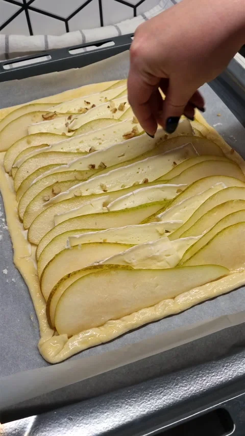 Vertical view of hand sprinkling crushed walnuts on uncooked pear brie tart. Stock-Footage 347747854