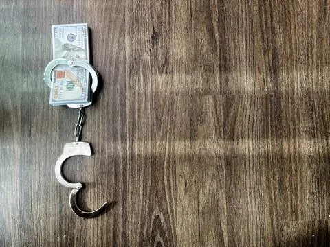 Vertical view of handcuffs locked around a stack of hundred dollar bills on.. Stock Photos