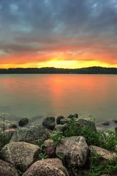 Vertical view on the lake with dark clouds on the sky and big smooth stones. Stock Photos