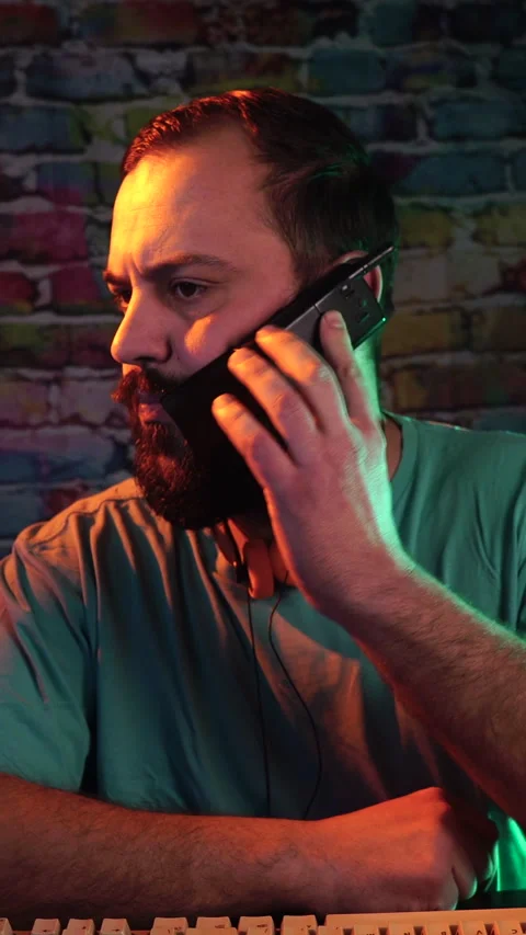 Vertical View of Man Making Phone Call With Flip Cellphone in Front of Monitor Stock Footage 301882792