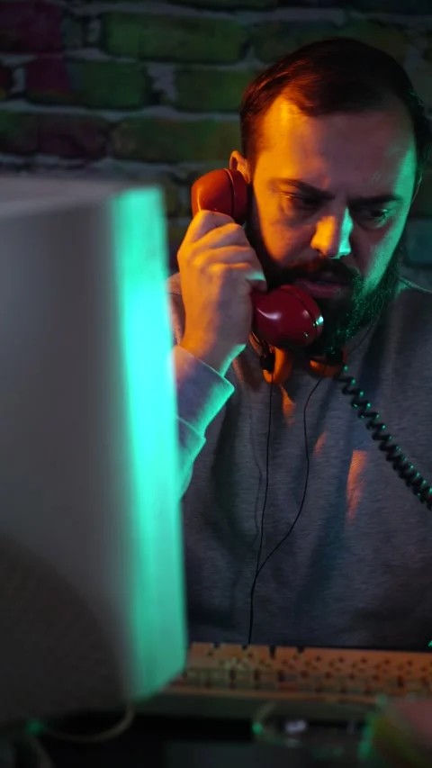 Vertical View of Man Talking Over Landline Telephone in Front of Flickering CRT Stock Footage 302416730