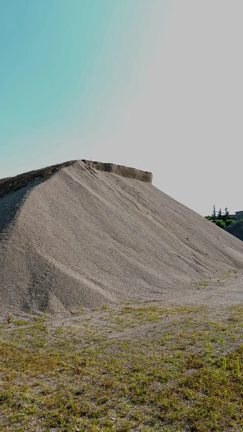 Vertical view of massive grey gravel pile against blue sky with green grass Stock Footage 343790200