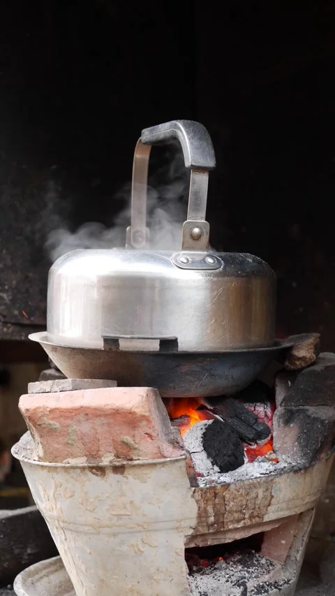 Vertical view of a metal kettle heating on a clay stove where open fire and Stock Footage 331725907
