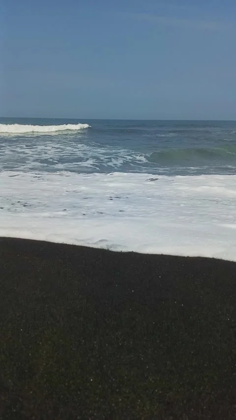 Vertical view of ocean surf and white waves washing over a dark volcanic san 스톡 동영상 340966098