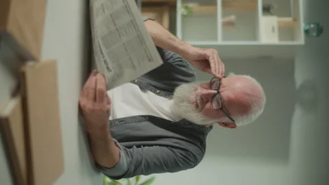 Vertical View.An Old Man in the Glasses Sits at a Table and Reads a Newspaper. Video stock 250300642