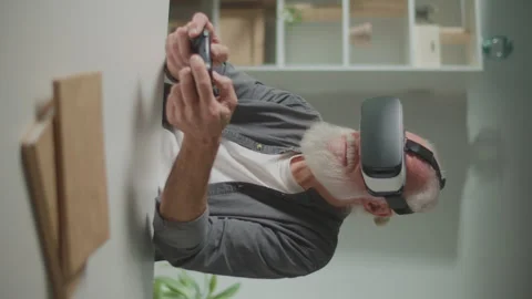 Vertical View.An Old Man in VR Glasses Plays Computer Games With a Joystick Video stock 249711406