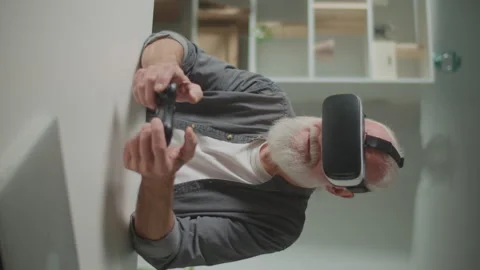Vertical View.An Old Man in VR Glasses Plays Computer Games With a Joystick Stock Footage 250303582