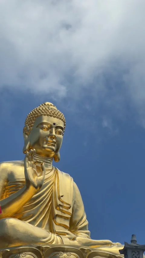 Vertical view shows golden Buddha statue with raised symbolic mudra gesture agai Stock Footage 341407876