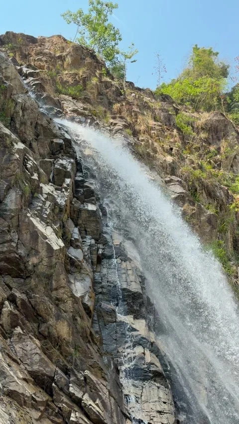 Vertical view shows a narrow stream sliding down a stone waterfall wall forming Stock Footage 335206391