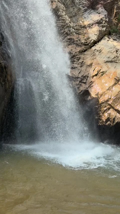 Vertical view shows a narrow waterfall stream falling down a rocky slope into a 스톡 동영상 341407957