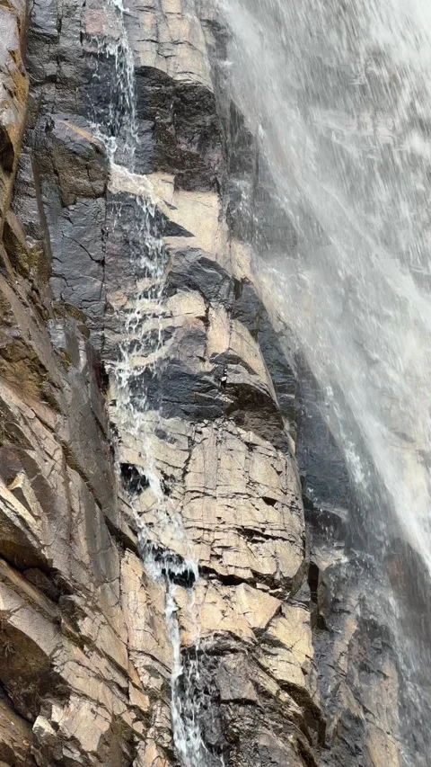 Vertical view shows a waterfall stream descending along a steep rocky cliff 库存影片 333256371