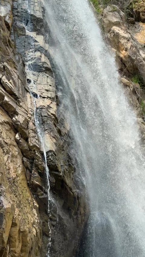 Vertical view shows a waterfall stream flowing down a steep rock surface forming Stock Footage 335443069