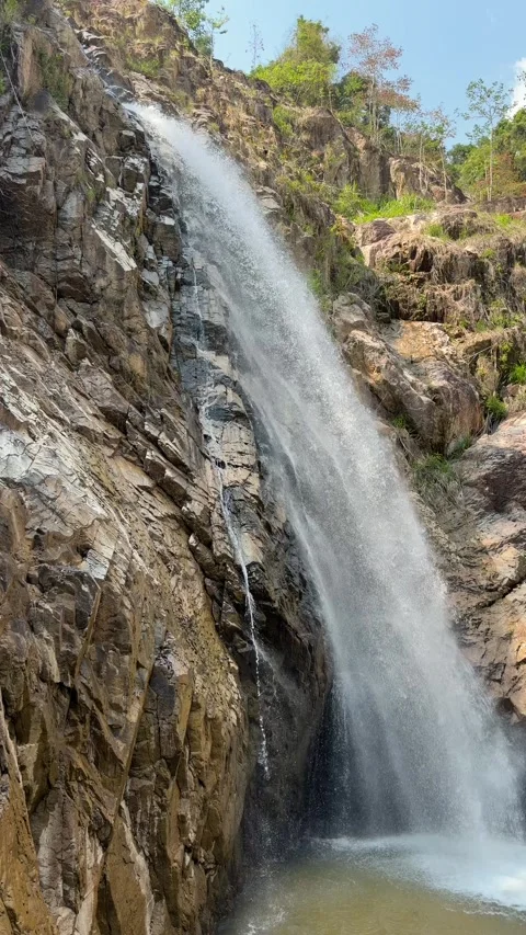 Vertical view shows a waterfall stream descending into a rocky basin forming a Stock Footage 336236856