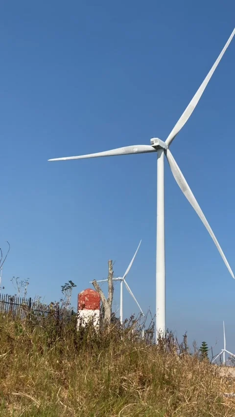 Vertical view shows a wind turbine rotating on a hill beneath a wide sky forming Stock Footage 335206368