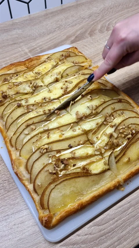 Vertical view of slicing baked pear brie puff pastry tart with knife on cutting 스톡 동영상 347747673