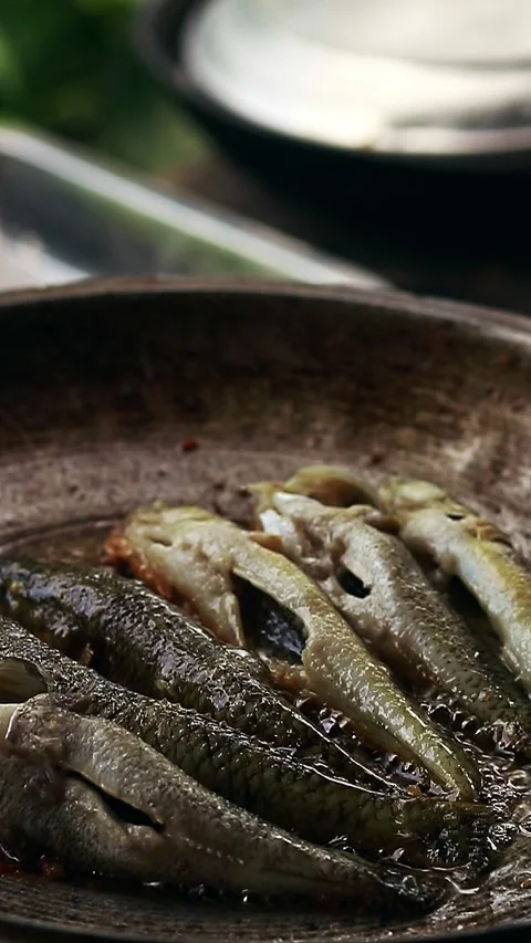 Vertical view of small herring or tamban frying in an iron skillet Stock Footage 251728282