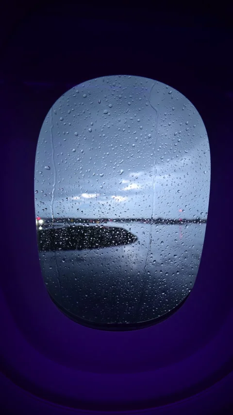 Vertical view through a rain-streaked airplane window of a dark wet airport Stock Footage 342285303