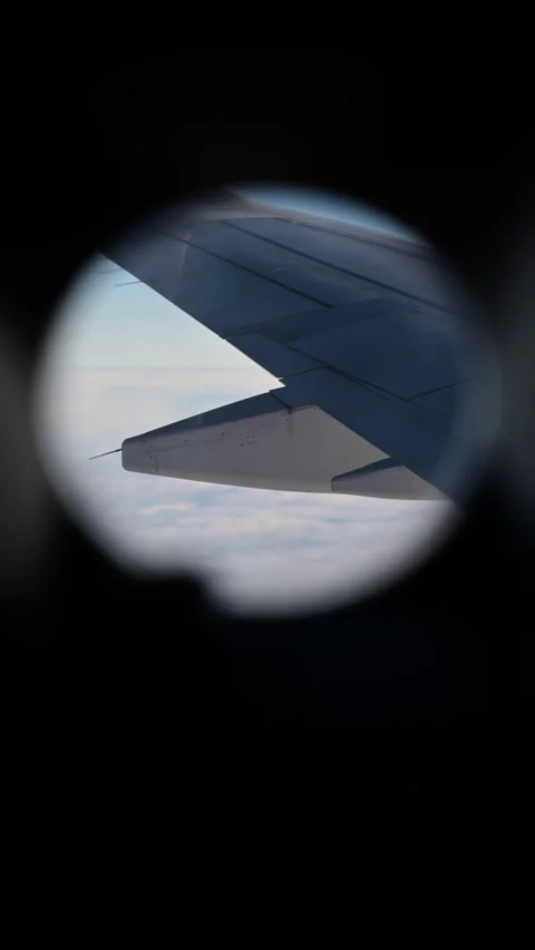 Vertical view through a round cabin window of an airplane wing above a white Video stock 342251083