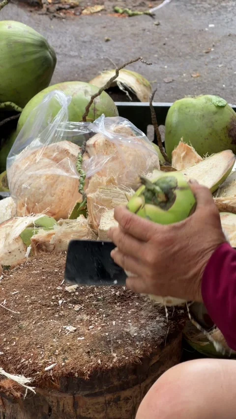 Vertical view of a vendor cutting open a coconut with a machete on a wooden Stock-Footage 330522970