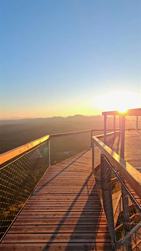 Vertical view walking down wooden lookout tower walkway at sunrise in mountains. 스톡 동영상 348243040