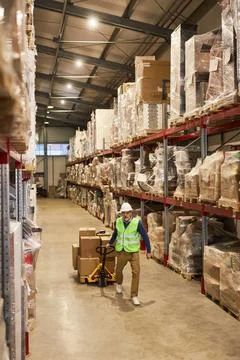 Vertical view at warehouse interior with worker pulling cart in row aisle Stock Photos