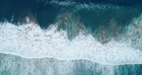 Vertical view of waves breaking just before the shore leaving trails of bubbl Stock Footage 87573555