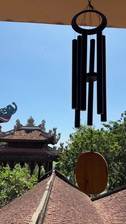 Vertical view of a wind bell swinging near tree canopy and sky, showing delicate Stockbeeldmateriaal 333982196