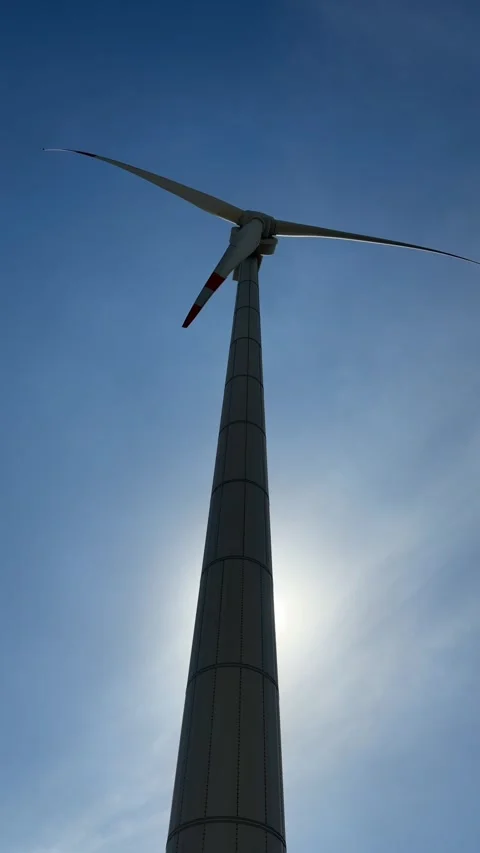 Vertical view of a wind turbine centered in frame, its blades rotating in front Vidéo 333198039