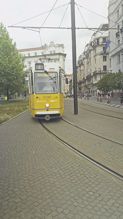 Vertical view of a yellow Budapest tram travelling along a paved city street in Stock Footage 345284248