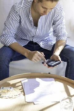 Vertical view of young man sitting in the couch doing calculations and paperw 스톡 사진