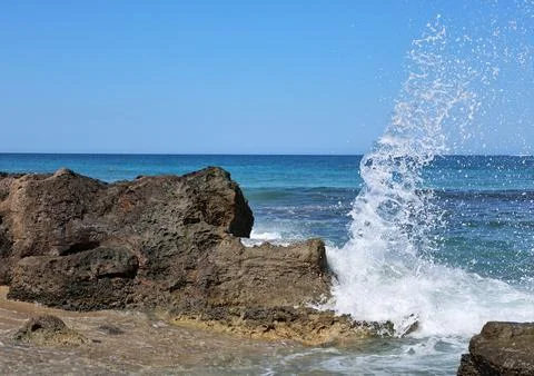 Vertical wave explosion over Crete coastal rocks with sea spray and blue sky Stock Photos
