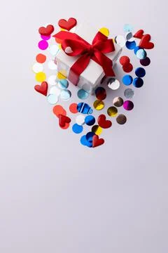 Vertical of white gift box with red ribbon on heart shape of confetti, white Foto stock
