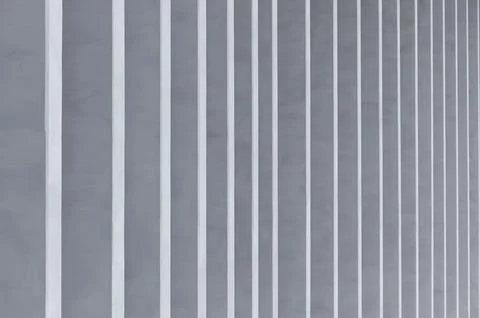 Vertical white stripes on a gray wall create a minimalist abstract pattern. Stock Photos