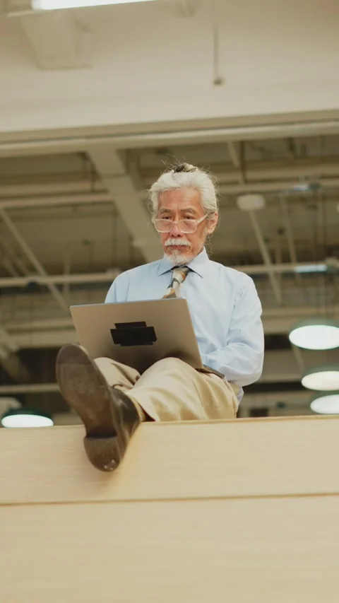 Vertical wide low angle of senior Thai man using laptop atop wooden bleachers 스톡 동영상 347776748