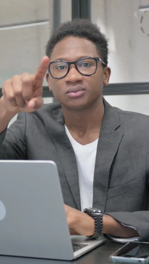 Vertical, Young African Man Pointing at Camera while Working on Laptop Vídeo Stock 325560194