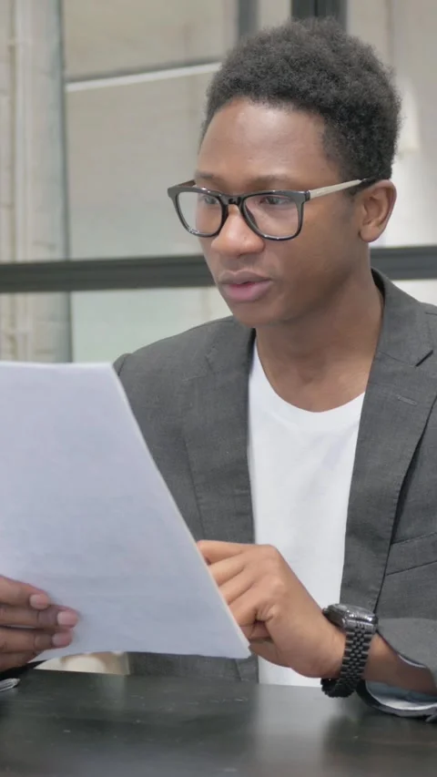 Vertical, Young African Man Reading Documents at Work 動画素材 325560726
