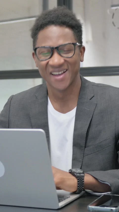 Vertical, Young African Man Smiling at Camera while Working on Laptop in Office Video stock 325560176